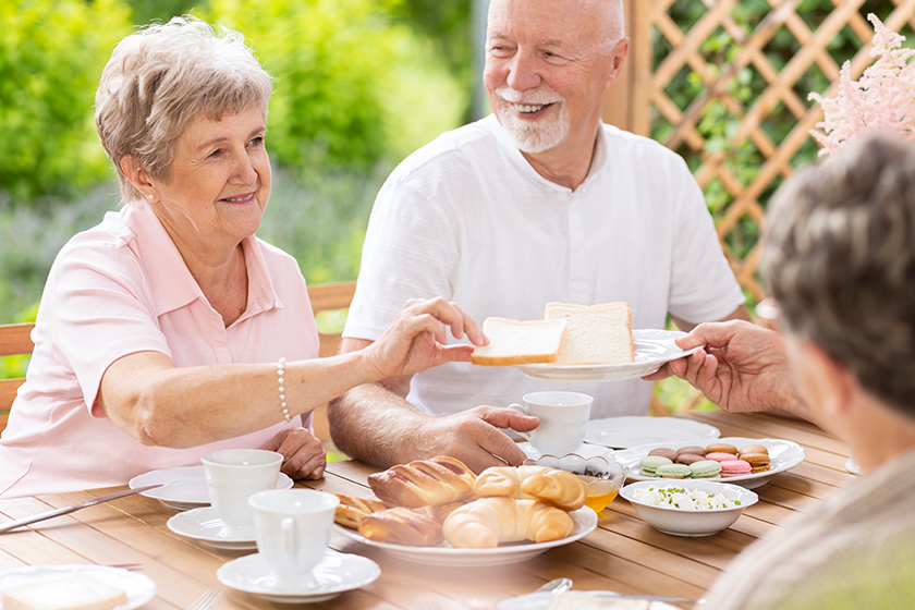 Smiling grandmother eating breakfast with friends on the terrace 